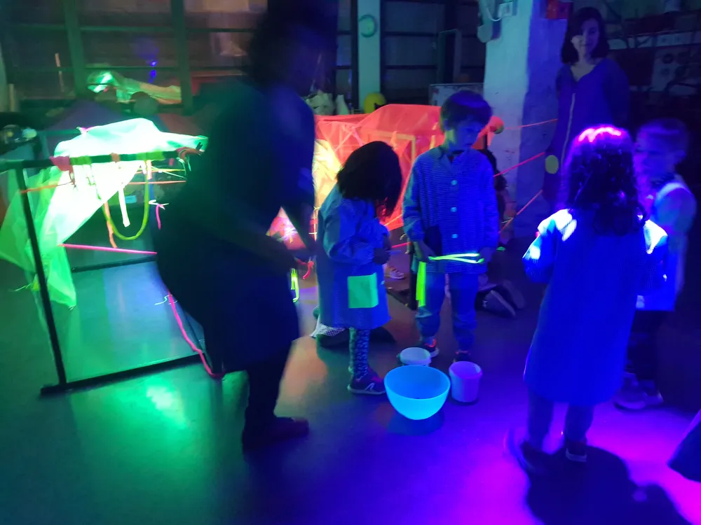 Infants jugant amb objectes fluorescents en una sala il·luminada amb llum negra verda i lila