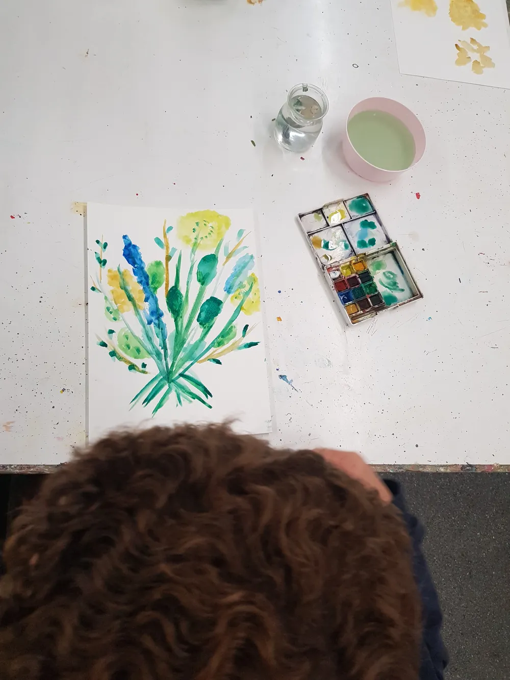 Pintura d’aquarel·la d’una planta damunt d’una taula, amb la capsa de colors al costat