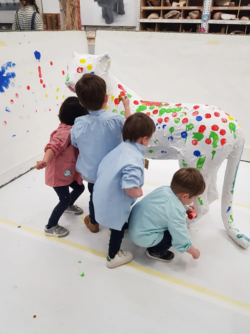 Un grup d’infants pintant de punts de colors una escultura blanca en forma d’animal