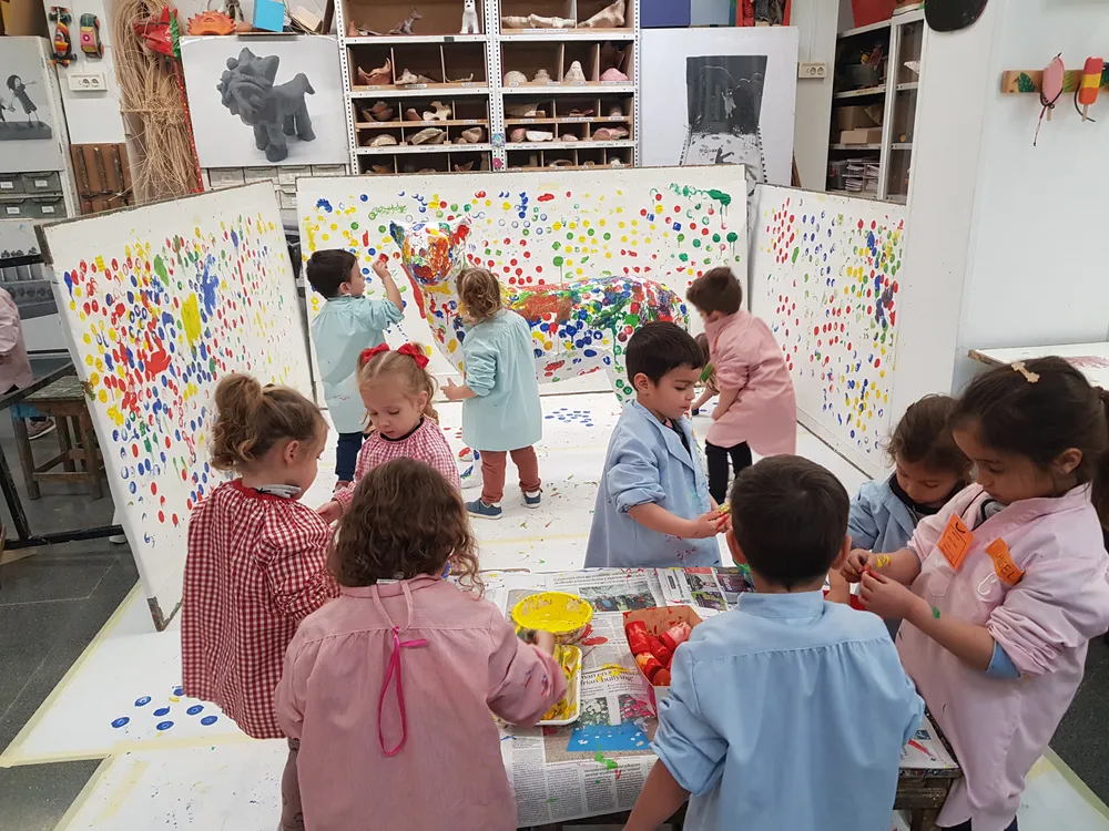 Infants pintant grans murals de punts de colors sobre paper blanc en un taller de l’escola Traç